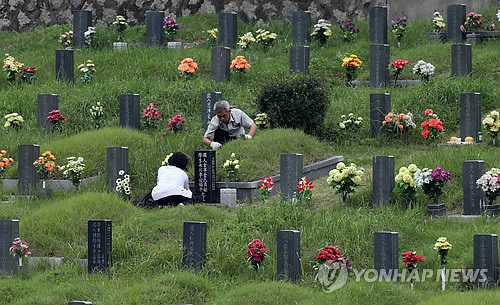 到釜山永乐公园扫墓的人络绎不绝，图为一对老夫妇在整理墓地。（图片来源：韩联社）