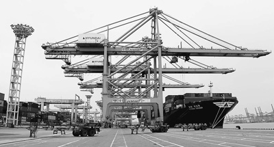 4月12日，釜山港码头上的龙门吊正在把货轮上的集装箱搬运到一辆辆货柜车上。（本报记者 陈尚文摄）