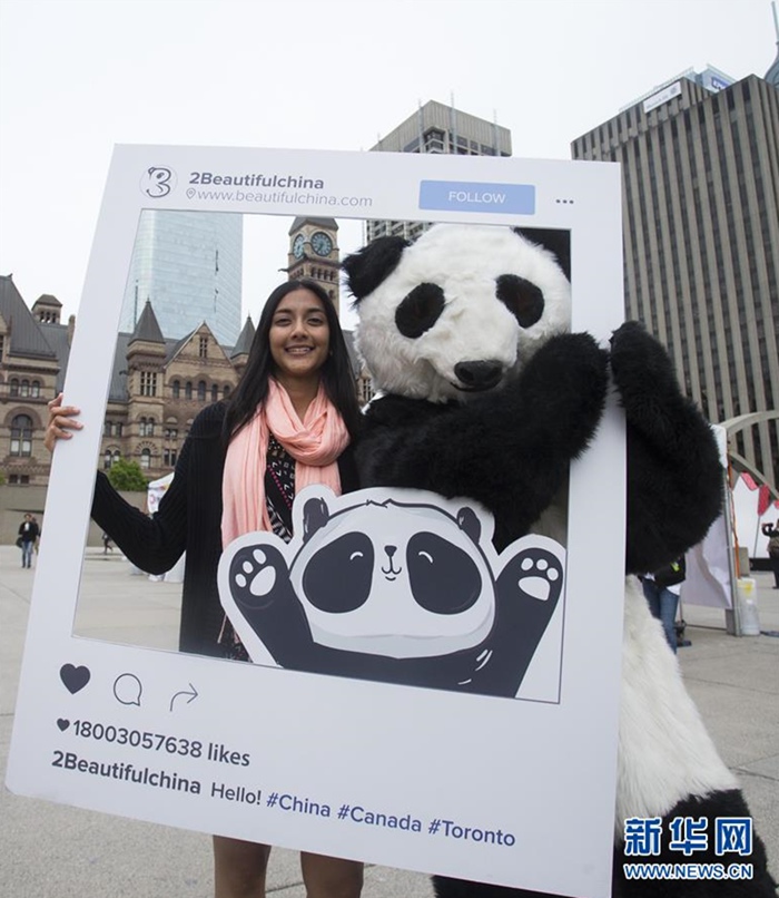 這是2017年5月19日，在加拿大多倫多市政廣場，一名游客在中國旅游文化節上與熊貓人偶合影。主題為“熊貓走世界——美麗中國”的2017年加拿大中國旅游文化節當日在多倫多市政廣場舉行。新華社發（鄒崢 攝）