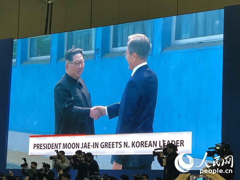 當地時間27日上午9時30分許，朝鮮最高領導人金正恩在板門店跨過軍事分界線，與韓國總統文在寅會晤。兩位領導人在軍事分界線握手，開始歷史性的會面。圖為在韓國高陽媒體中心拍攝的電視直播畫面。夏雪攝
