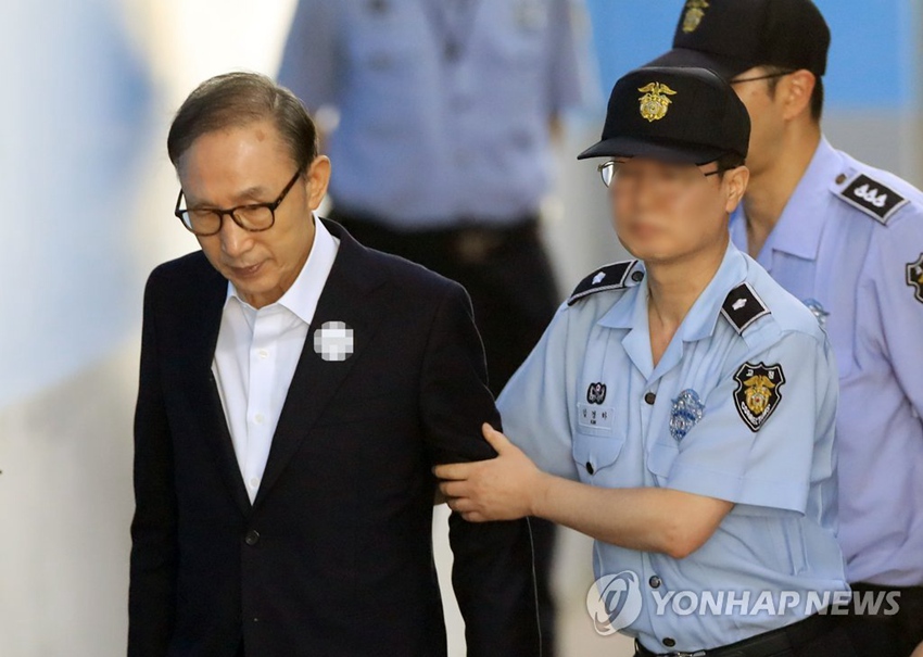當地時間15日上午，韓國前總統李明博在獄警攙扶下，前往首爾中央地方法院出庭受審。（圖片來源：韓聯社）