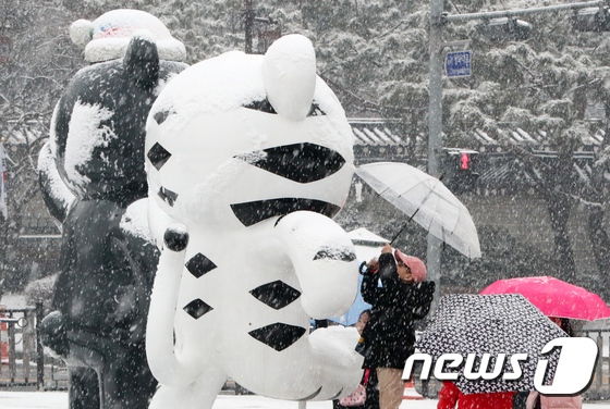19日在首尔青瓦台喷水池附近，一儿童为摆放在此处的平昌冬奥会吉祥物撑伞遮雪。