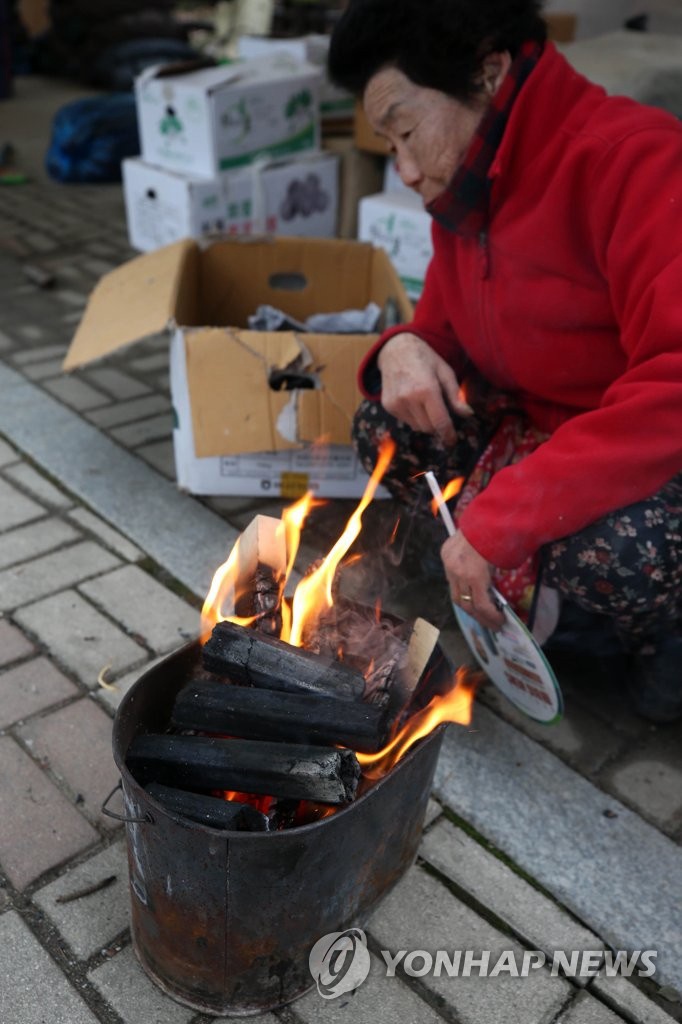 今日早晨在江原道春川市的某個市場，一位小販商人在路邊點火取暖。
