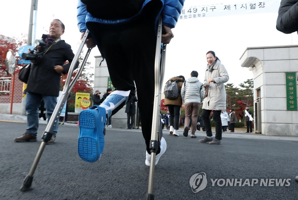14日上午，在江原春川高中，一位因腿部受傷拄著拐杖的考生向考場緩慢走去。