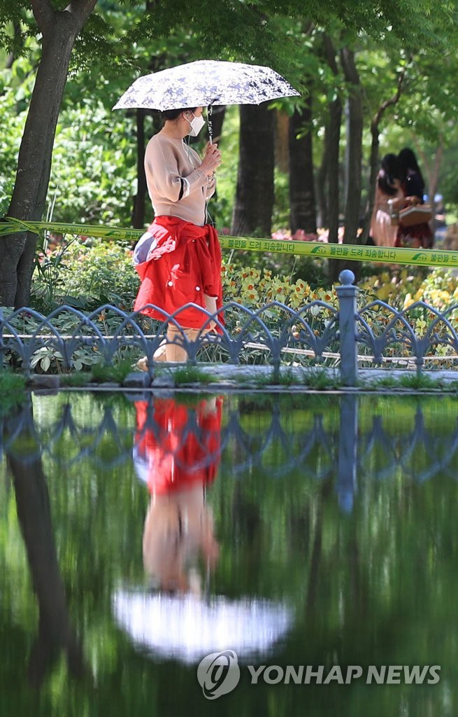5月6日，在“首爾林”公園，一位行人撐著太陽傘站在池塘邊上。