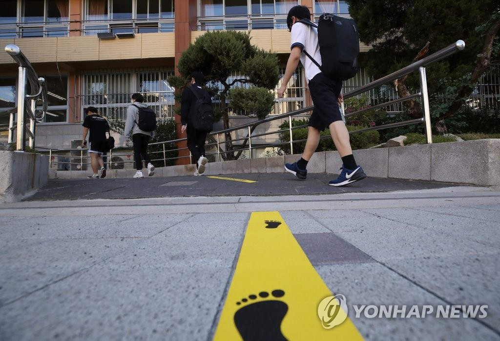 在首爾永登浦區汝矣島高中，學生們保持安全間距排成一列，按照規定路徑有序進入教室。