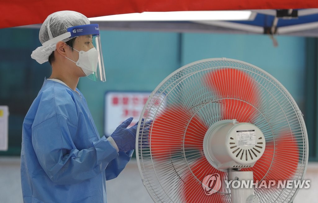 16日下午，在首爾中浪區醫療院篩查診療所內，醫務人員正在對著風扇降溫。