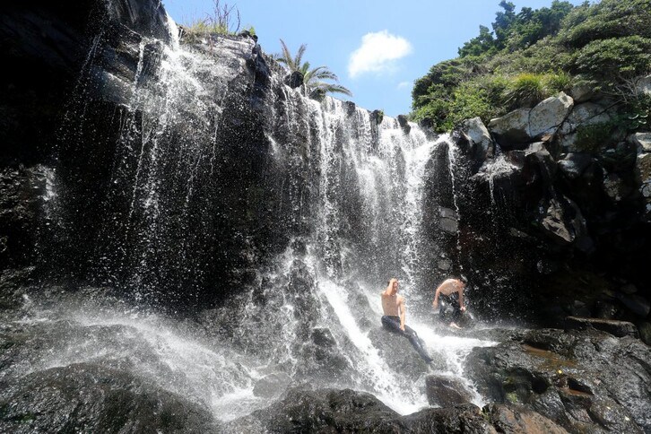 6月23日，济州西归浦市的某瀑布前，几名潜水者运动后坐在石阶上享受瀑布的清凉。
