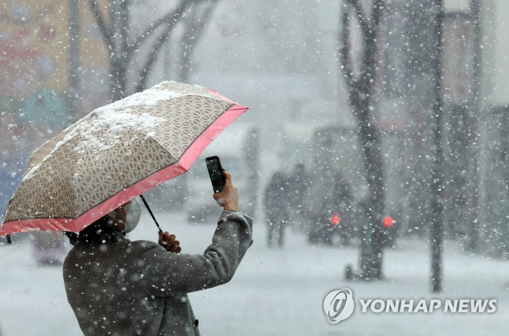 1月18日上午，一位市民撑着雨伞在首尔明洞街头拍照。