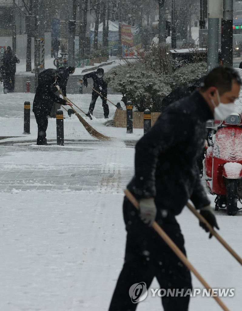 1月18日上午，在首尔明洞附近的大楼前，工作人员正在除雪。