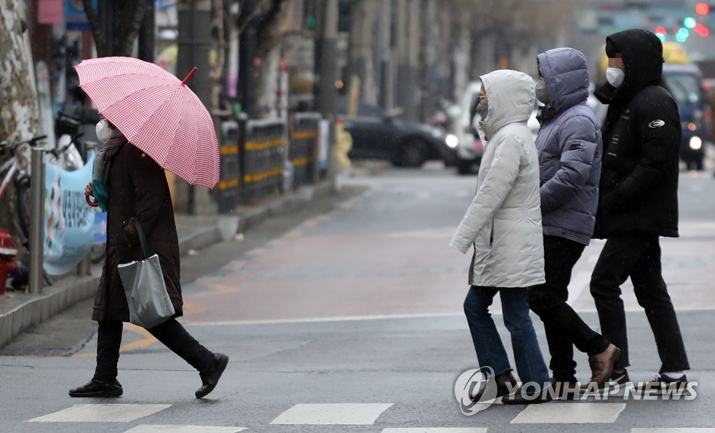 21日，首爾市，一位市民撐著雨傘，沒帶雨傘的市民則戴起帽子擋雨。