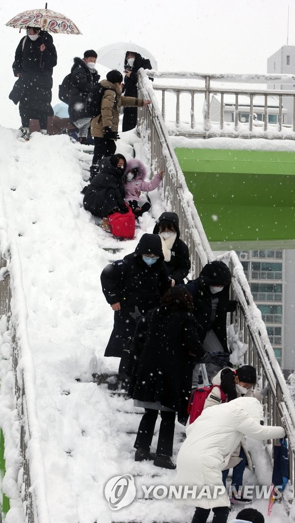 3月2日上午，在江原道江陵市，大雪覆蓋上學路，小學生和家長們小心翼翼地扶著欄杆走下天橋。江原道地區前一日降大雪。圖源：韓聯社