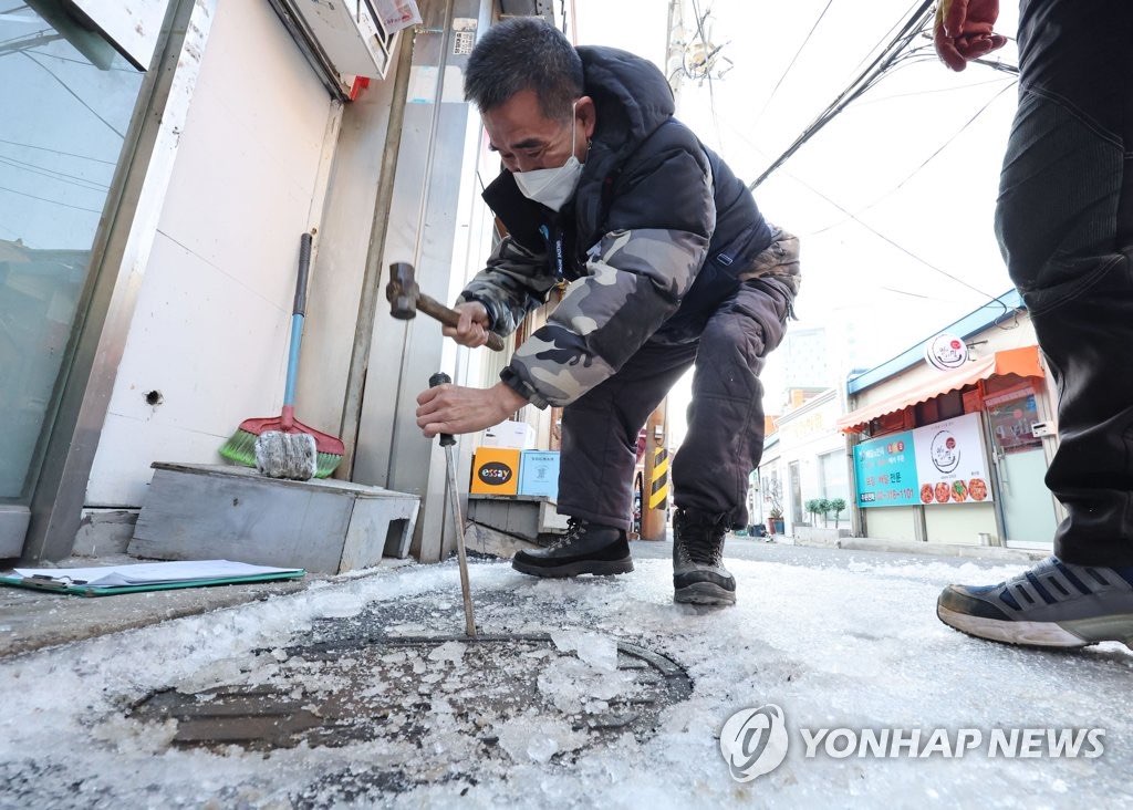 12日下午，在首尔市一栋建筑物前，一名工作人员正在破冰，检查被冻坏的自来水管。