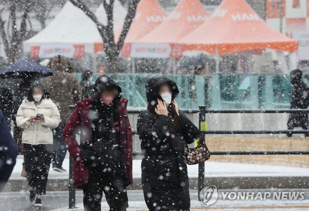 19日上午，首尔光化门路口，当地市民冒着鹅毛大雪过马路。