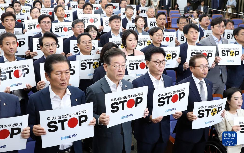 8月24日，韩国最大在野党共同民主党党首李在明（前排左二）与议员在首尔国会举行的紧急会议上手举标语，抗议日本核污染水排海。
