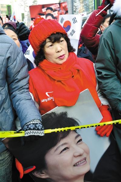韩民调:大选当前 两方均力敌 选民首要关注经济 12月13日，韩国执政党新国家党总统候选人朴槿惠举行竞选活动时，一支持者手持其画像。