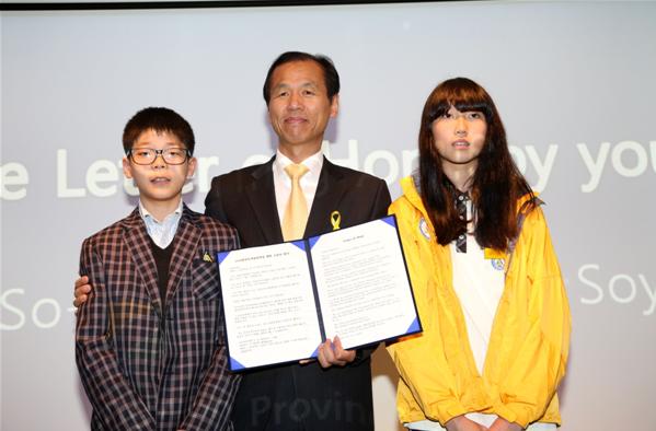 学生们在2014年4月28日召开的2018年平昌冬奥会赛场建设促进情况新闻发布会上朗读信件，祝愿冬奥会成功举办。江原道知事崔文洵与学生们合影留念。